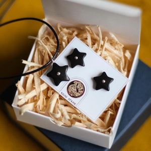 May include: A black star-shaped necklace and earrings set in a white gift box with a black and gold logo that says "Коло Птахи".