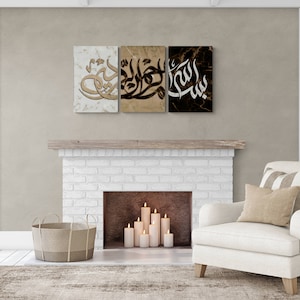 May include: Three framed canvas prints with Arabic calligraphy in black and gold on a marble background. The prints are hung above a white brick fireplace with candles inside.