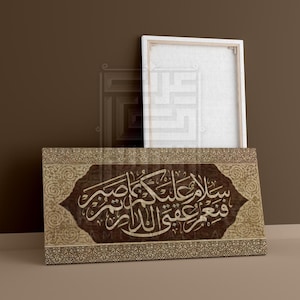May include: A decorative canvas print featuring Arabic calligraphy in white script on a brown background. The print has a decorative border and is leaning against a blank white canvas.
