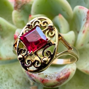 May include: A gold ring with a red gemstone set in a filigree design.