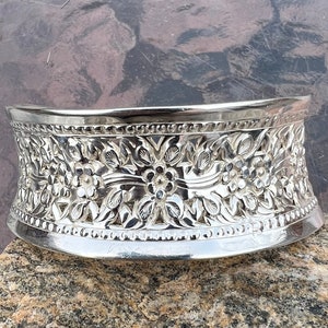May include: A silver, decorative, floral patterned cake stand. The stand is round and has a raised edge.