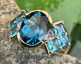 May include: A gold ring with a large oval blue topaz gemstone surrounded by smaller blue topaz stones.