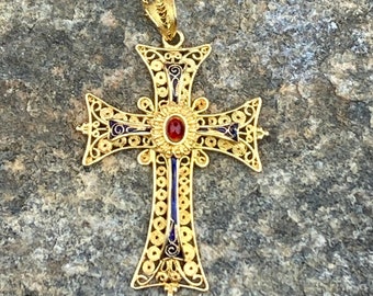 May include: A gold filigree cross pendant with a red gemstone in the center. The cross is decorated with blue enamel and hangs from a gold chain.