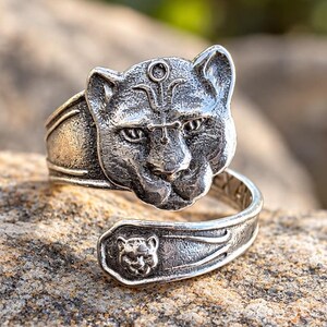 May include: A silver-toned metal wrap ring featuring a detailed sculpted panther head on one end and a smaller, secondary panther head embossed on the opposite tapered end. The surface has an oxidized finish to highlight the feline facial features.
