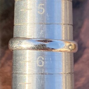 Pu&ograve; includere: Un anello d'argento che viene misurato su un misuratore di anelli in metallo. Il misuratore di anelli mostra che la misura dell'anello &egrave; un 6.