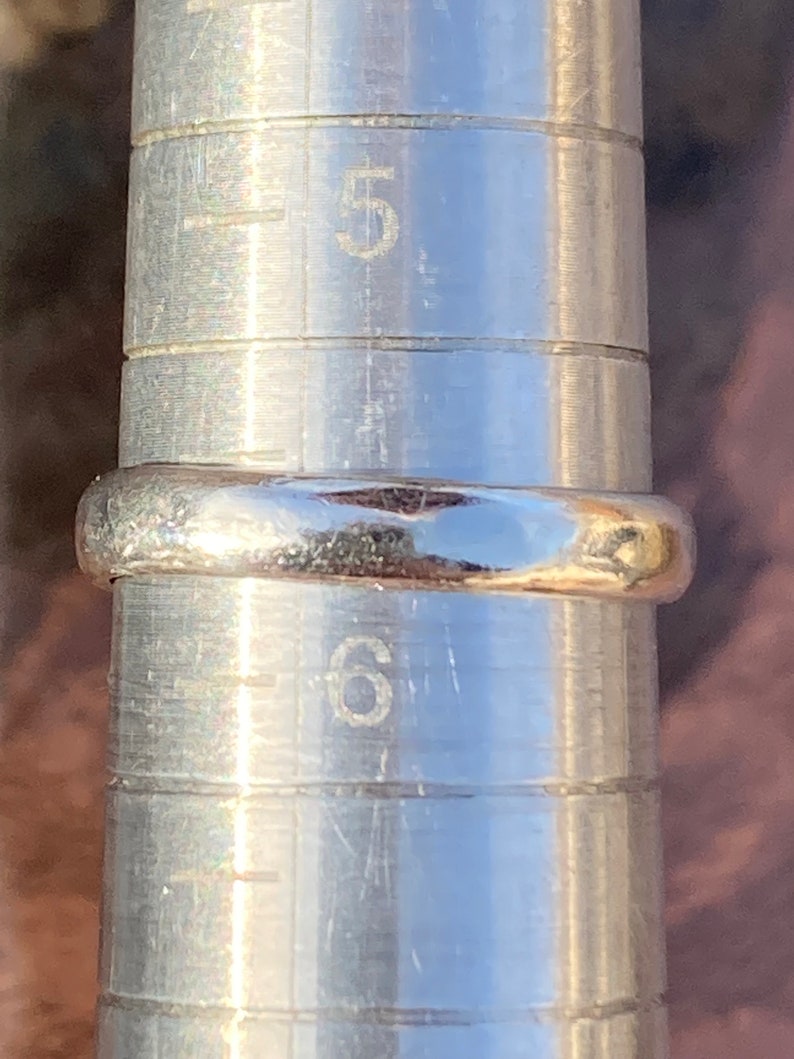 Pu&ograve; includere: Un anello d'argento che viene misurato su un misuratore di anelli in metallo. Il misuratore di anelli mostra che la misura dell'anello &egrave; un 6.