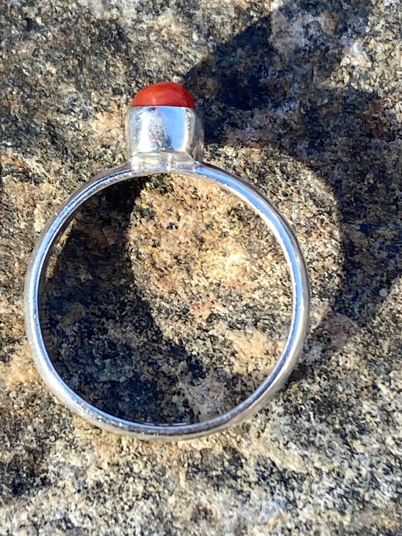 Pu&ograve; includere: Un anello d'argento con una pietra preziosa rossa al centro.