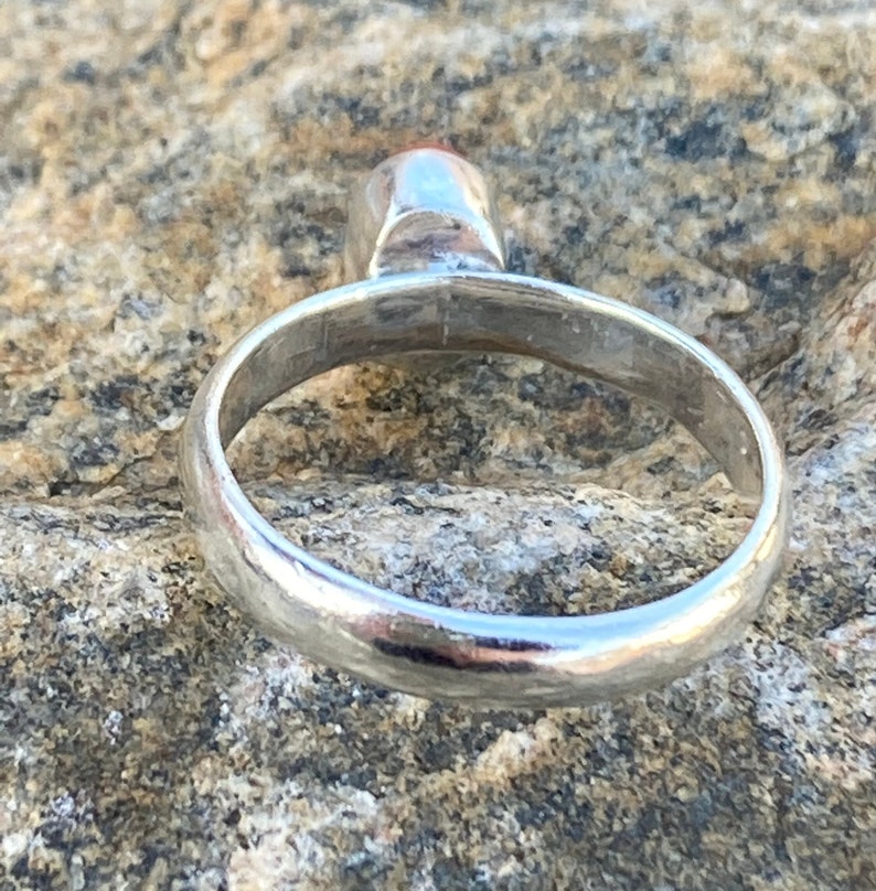 Pu&ograve; includere: Un anello d'argento con una fascia liscia e arrotondata. L'anello &egrave; mostrato di lato, con la parte superiore della fascia rivolta verso lo spettatore.