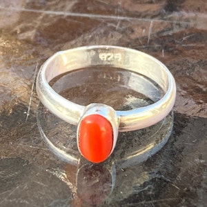 Pu&ograve; includere: Un anello d'argento con una pietra di corallo ovale di colore arancione brillante. L'anello &egrave; contrassegnato dal numero "925" sulla fascia interna.