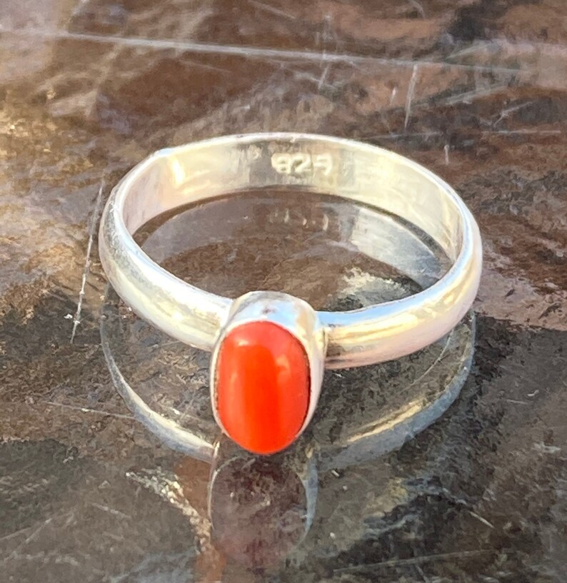 Pu&ograve; includere: Un anello d'argento con una pietra di corallo ovale di colore arancione brillante. L'anello &egrave; contrassegnato dal numero "925" sulla fascia interna.