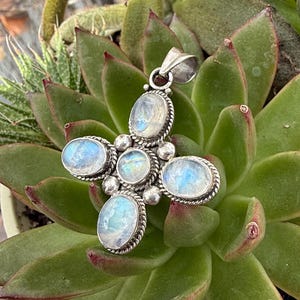 May include: A silver pendant with a cross design featuring five iridescent moonstone stones.