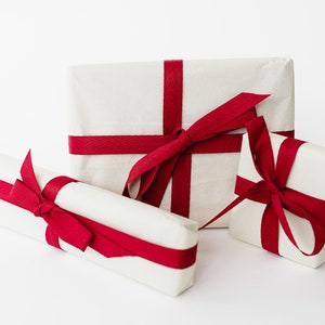 May include: Three white gift boxes wrapped with red ribbon bows. The boxes are of different sizes and are arranged on a white surface.