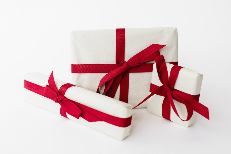 May include: Three white gift boxes wrapped with red ribbon bows. The boxes are of different sizes and are arranged on a white surface.