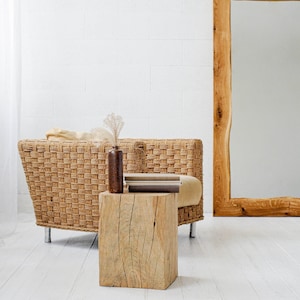 Könnte beinhalten: Ein geflochtener Korbstuhl mit einem Holzsockel und ein Holzhocker mit einem Stapel Bücher darauf. Der Stuhl und der Hocker stehen vor einem großen, mit Holz gerahmten Spiegel.