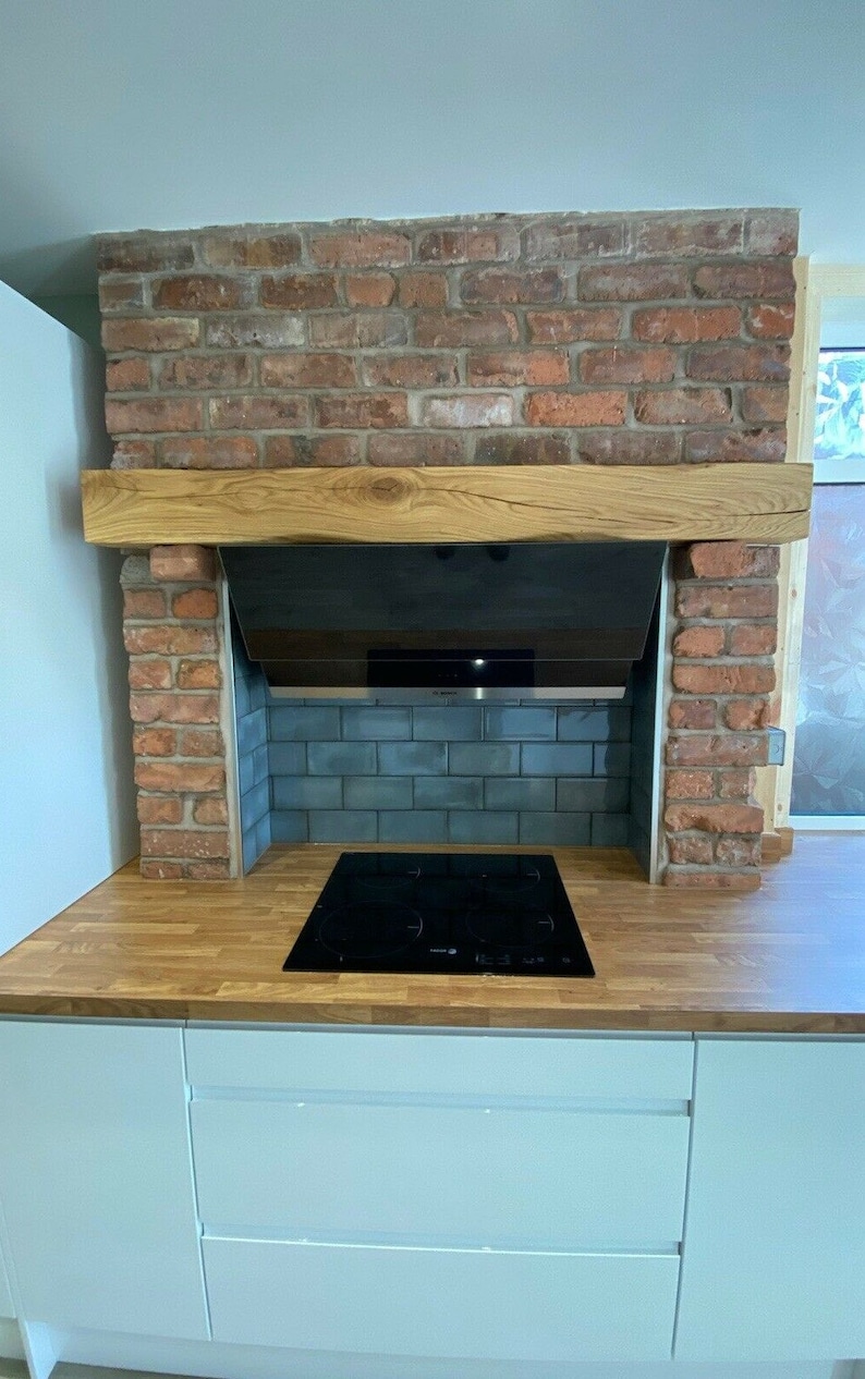 May include: A modern kitchen with a black electric stovetop, a wood countertop, and a brick fireplace with a wooden mantel. The fireplace has a black vent hood and blue tile surround.