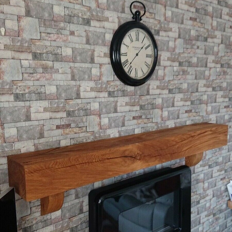 May include: A wooden mantel shelf with a distressed finish, mounted above a black fireplace. The shelf is supported by two brackets. A black clock with Roman numerals is hanging on the wall above the shelf.