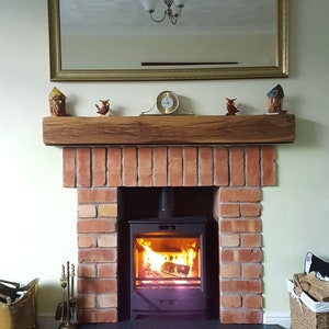 May include: A brick fireplace with a wood-burning stove. The stove has a glass door and is burning a fire. The fireplace has a wooden mantel with decorative items on it.