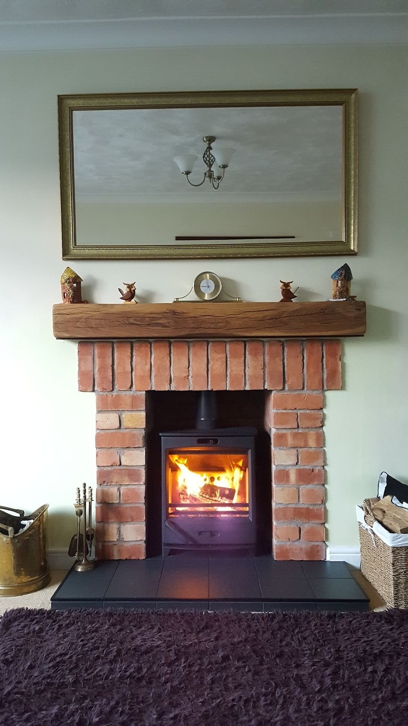 May include: A brick fireplace with a wood-burning stove. The stove has a glass door and is burning a fire. The fireplace has a wooden mantel with decorative items on it.