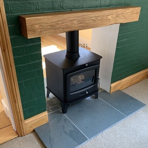 May include: A black wood-burning stove with a glass door and a black pipe, set on a slate hearth in front of a green brick wall with a wooden mantel.