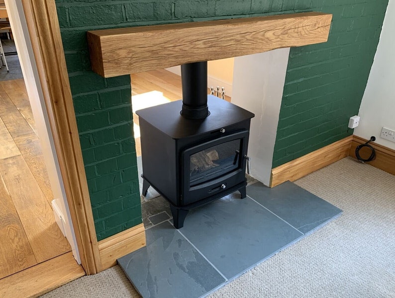 May include: A black wood-burning stove with a glass door and a black pipe, set on a slate hearth in front of a green brick wall with a wooden mantel.