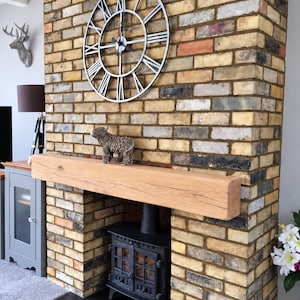 May include: A thick, rectangular natural light-brown wooden mantelpiece mounted on a multi-colored brick fireplace wall. The mantel features visible wood grain and natural cracks, positioned above a black metal wood-burning stove.