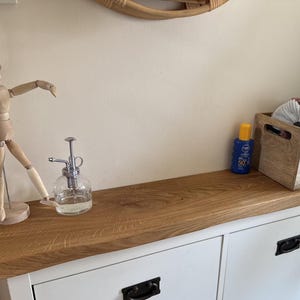 May include: A wooden articulated mannequin wearing a knitted hat stands on a white cabinet with a natural wood top. A glass spray bottle and a blue sunscreen bottle are also on the cabinet. A wooden box contains various items.