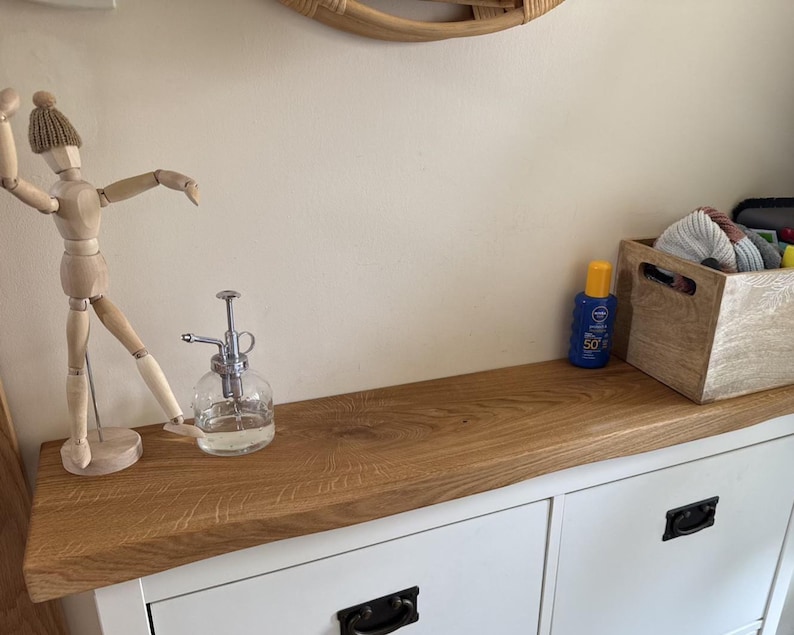 May include: A wooden articulated mannequin wearing a knitted hat stands on a white cabinet with a natural wood top. A glass spray bottle and a blue sunscreen bottle are also on the cabinet. A wooden box contains various items.