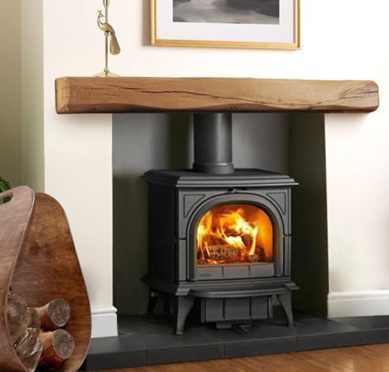 May include: A black wood-burning stove with a glass door and a fire burning inside. The stove is set into a fireplace with a wooden mantel above it.