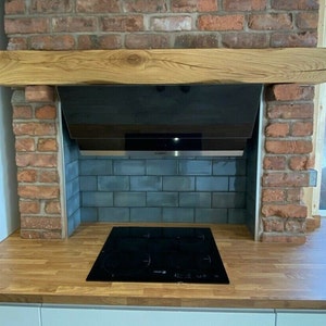 May include: A modern kitchen with a brick fireplace and a black stovetop. The stovetop is set into a wooden countertop with a wooden beam above it. The backsplash is made of blue tiles.