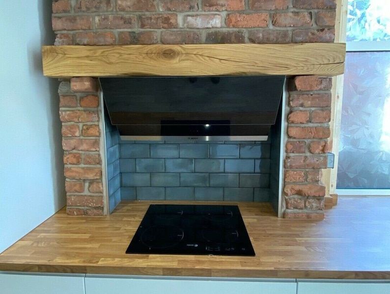 May include: A modern kitchen with a brick fireplace and a black stovetop. The stovetop is set into a wooden countertop with a wooden beam above it. The backsplash is made of blue tiles.