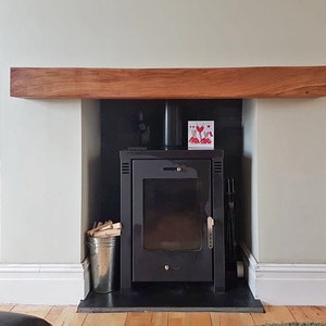 May include: A black wood-burning stove with a glass door and a black metal frame. The stove is set into a white fireplace with a wooden mantel. There is a card with red hearts on it above the stove.