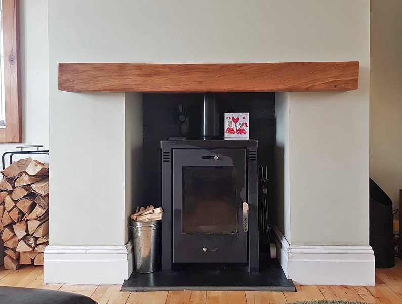 May include: A black wood-burning stove with a glass door and a black metal frame. The stove is set into a white fireplace with a wooden mantel. There is a card with red hearts on it above the stove.