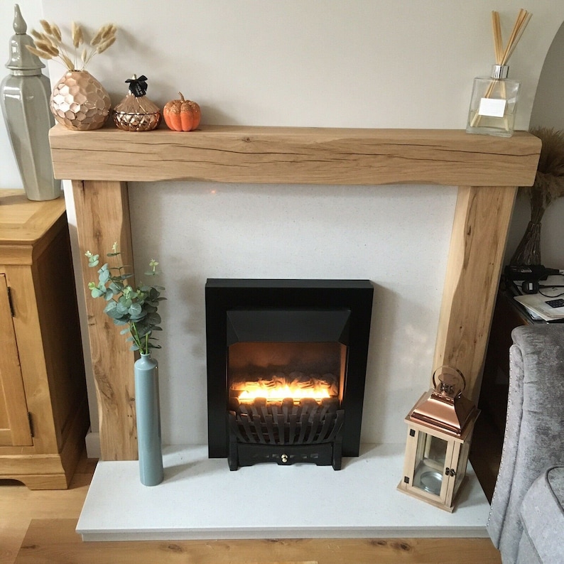 May include: A white fireplace mantel with a wooden beam, a black electric fireplace insert, and a decorative lantern. The mantel is decorated with fall-themed pumpkins and a vase of eucalyptus.