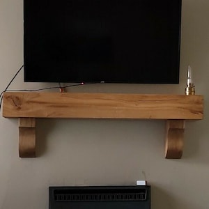 May include: A wooden mantel shelf with a flat top and decorative scrollwork on the sides. A flat screen TV is mounted above the shelf.