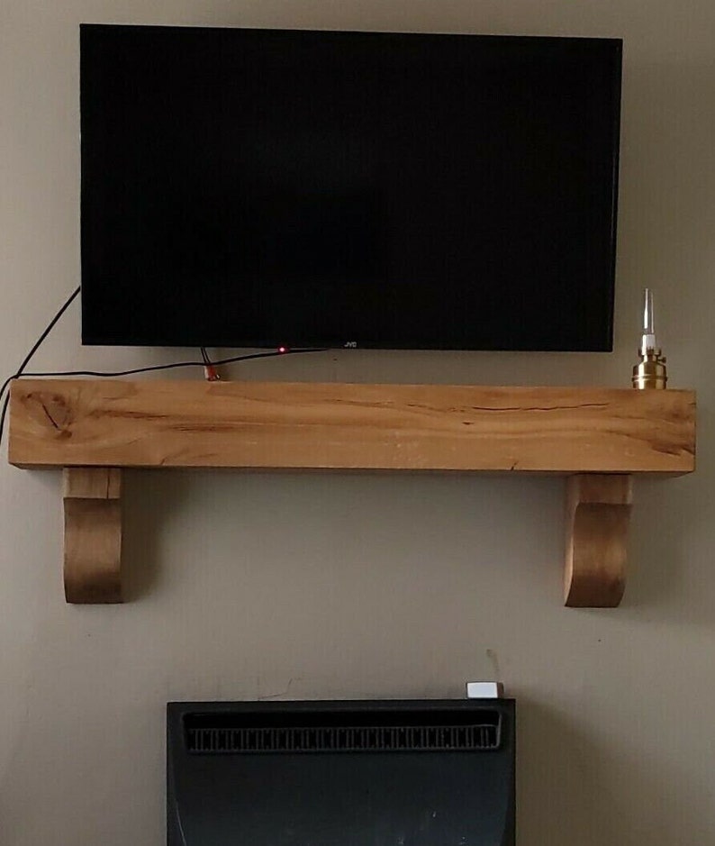 May include: A wooden mantel shelf with a flat top and decorative scrollwork on the sides. A flat screen TV is mounted above the shelf.