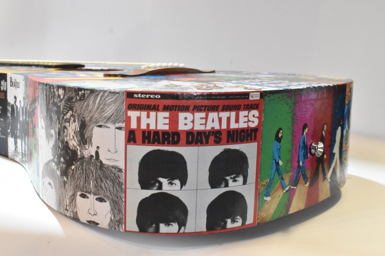 May include: A custom-made acoustic guitar featuring a Beatles theme. The body of the guitar is covered in album covers, including "A Hard Day's Night".