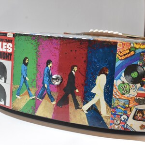 May include: A round, wooden box featuring a Beatles theme. The box is decorated with images from Beatles albums, including "Abbey Road" and "Yellow Submarine".
