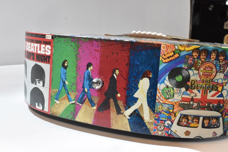 May include: A round, wooden box featuring a Beatles theme. The box is decorated with images from Beatles albums, including "Abbey Road" and "Yellow Submarine".