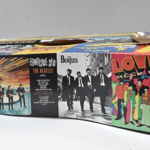 May include: A black acoustic guitar decorated with Beatles album covers. The covers include "Something New" and "Love Needs You".
