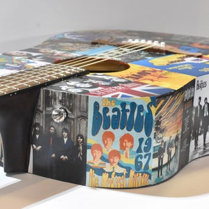 May include: A black acoustic guitar with a colourful collage of The Beatles album covers and images. The guitar has a natural wood finish and a black pickguard.