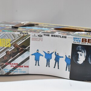 May include: A vintage acoustic guitar decorated with Beatles album covers. The guitar features album art from "Please Please Me", "Help!" and "Meet the Beatles".