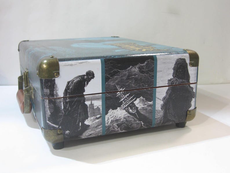 May include: A vintage-style, teal blue, rectangular suitcase with brass hardware and a printed design featuring a man in a long coat, a ship, and a figure in a long robe.