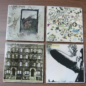May include: Set of four square ceramic coasters featuring album covers from Led Zeppelin. The coasters feature images of a man walking in a field, a building with windows, a blimp, and a colorful design with the band's name and album title "Led Zeppelin III".