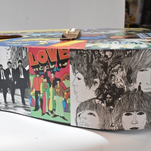 May include: A round, wooden acoustic guitar with a collage of Beatles album covers. The covers include "The Beatles", "Love", "A Hard Day's Night", and "Something New".