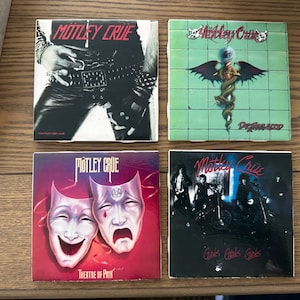 May include: Four square coasters featuring the band Motley Crue. Each coaster has a different album cover image. The coasters are black, white, and red with the band's name in white lettering. The album titles are "Too Fast For Love", "Dr. Feelgood", "Girls, Girls, Girls", and "Theatre of Pain".