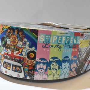 May include: A colourful acoustic guitar with a Beatles theme. The guitar is covered in images from various Beatles albums, including "Sgt. Pepper's Lonely Hearts Club Band" and "Abbey Road".