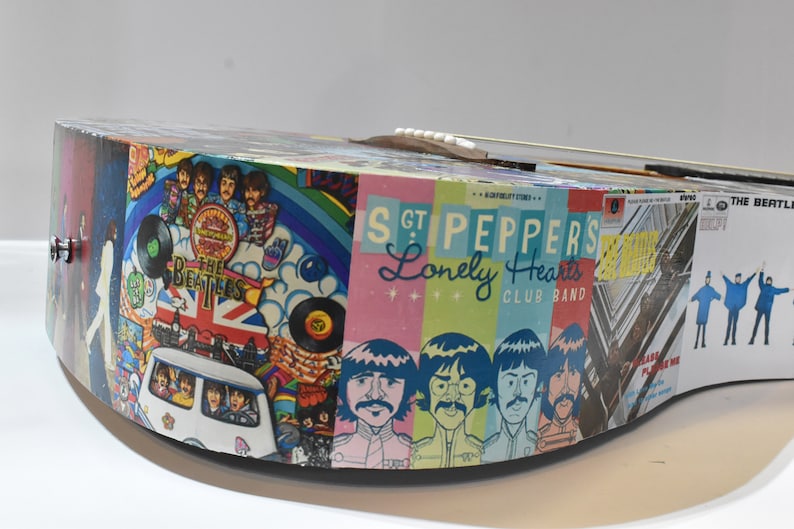 May include: A colourful acoustic guitar with a Beatles theme. The guitar is covered in images from various Beatles albums, including "Sgt. Pepper's Lonely Hearts Club Band" and "Abbey Road".