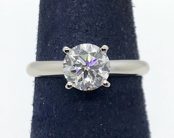 May include: A silver solitaire engagement ring with a large, round, brilliant-cut diamond.
