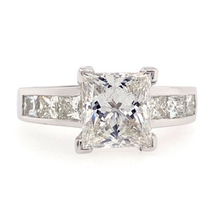 May include: A silver engagement ring with a large, square-cut diamond center stone and a band of smaller diamonds.