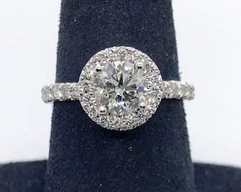 Könnte beinhalten: Ein silberner Verlobungsring mit einem großen runden Diamanten in der Mitte, umgeben von einem doppelten Heiligenschein aus kleineren Diamanten. Der Ring befindet sich auf einem schwarzen Samtringständer.
